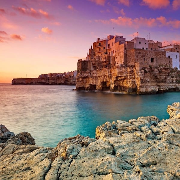 Coastal Italian town built into cliffs overlooking the turquoise sea under a vibrant sunset sky.