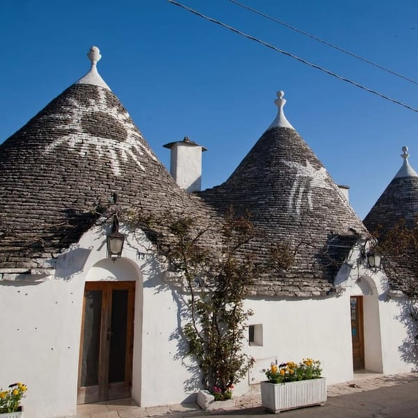 Traditional Italian trulli houses with conical stone roofs and white walls under a clear blue sky.