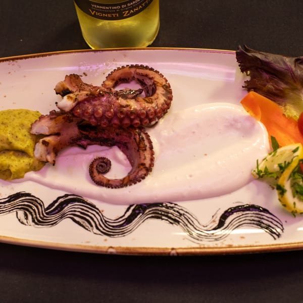 Grilled octopus with yellow and white sauces, garnished with lettuce, carrots, and lemon slices.