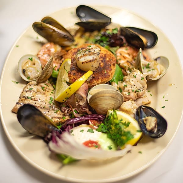 A plate of grilled seafood, including scallops, mussels, clams, and fish, garnished with lemon and herbs.