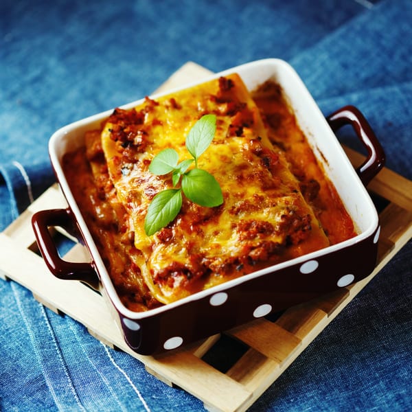 Baked Italian lasagna with melted cheese and fresh basil in a brown and white polka dot dish.