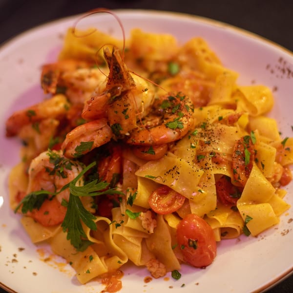 Pappardelle pasta with shrimp, cherry tomatoes, and fresh parsley on a white plate.